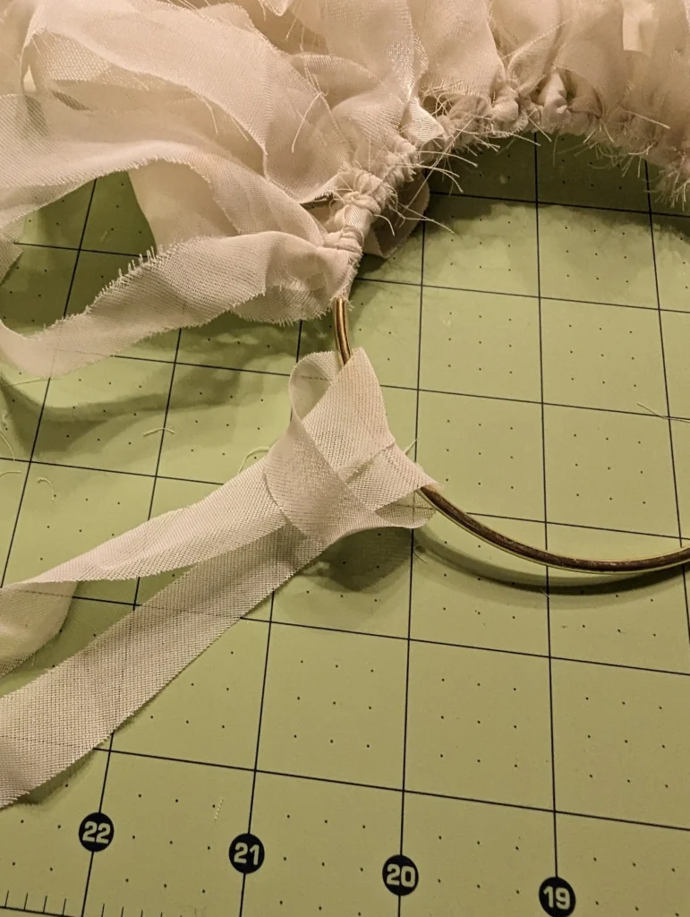 Ivory organza and taffeta strips cut from a mother's 1945 wedding dress being knotted onto a gold ring on a sewing cutting mat, the handmade process of healing grief after losing your mother