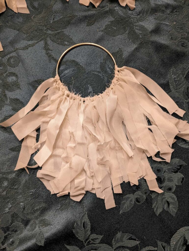 A handmade memorial ornament crafted from a mother's 1945 wedding dress, ivory organza and taffeta strips knotted through a gold ring, representing five siblings united in healing grief after losing your mother