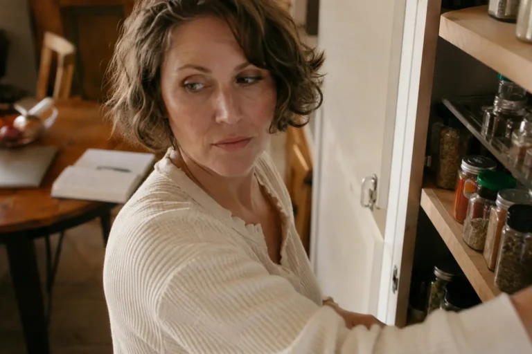A woman reorganizing her pantry instead of finishing a task, an everyday example of why you keep getting in your own way.
